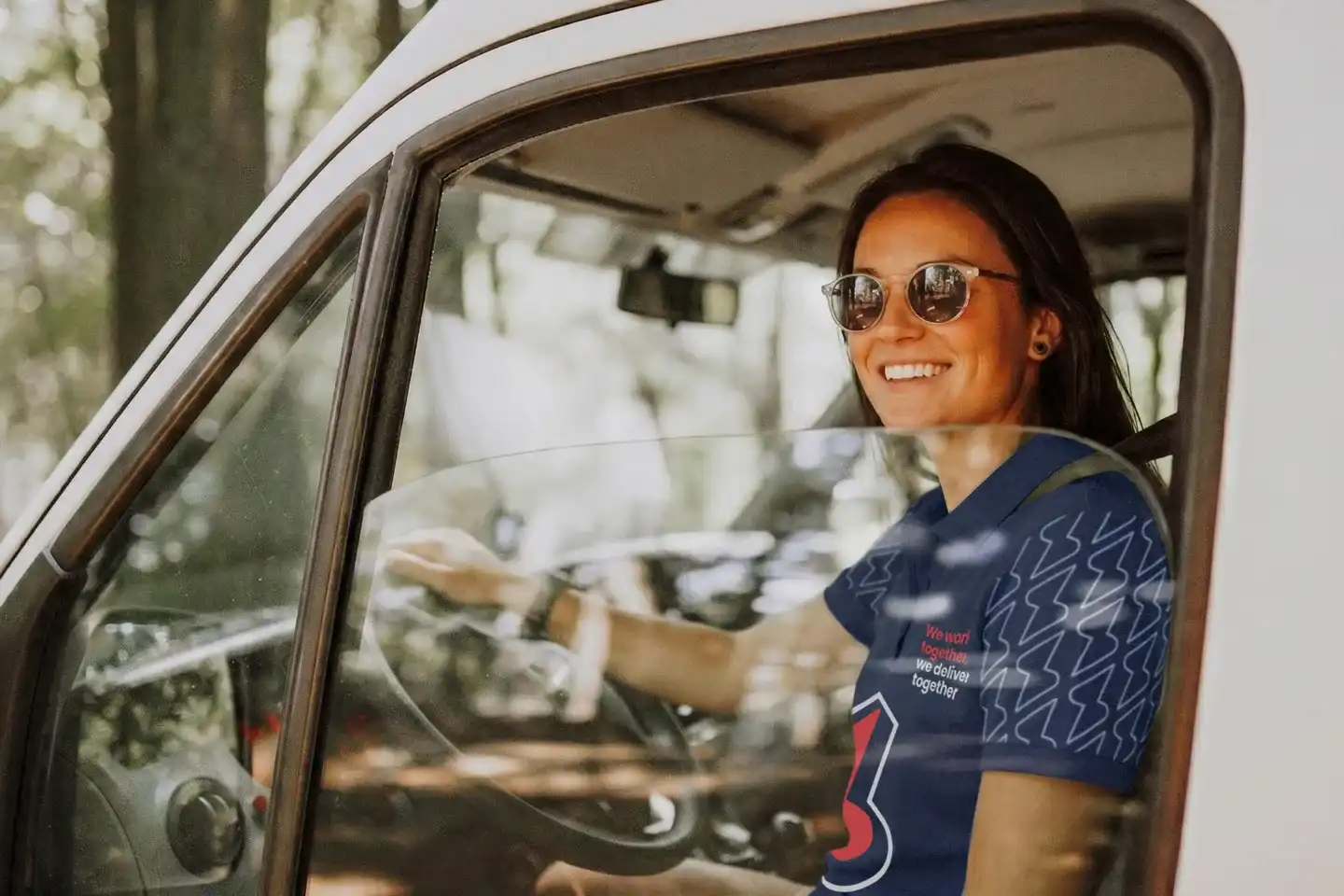 Conductora sonriendo al volante de una furgoneta blanca de reparto, con el polo de Service Club